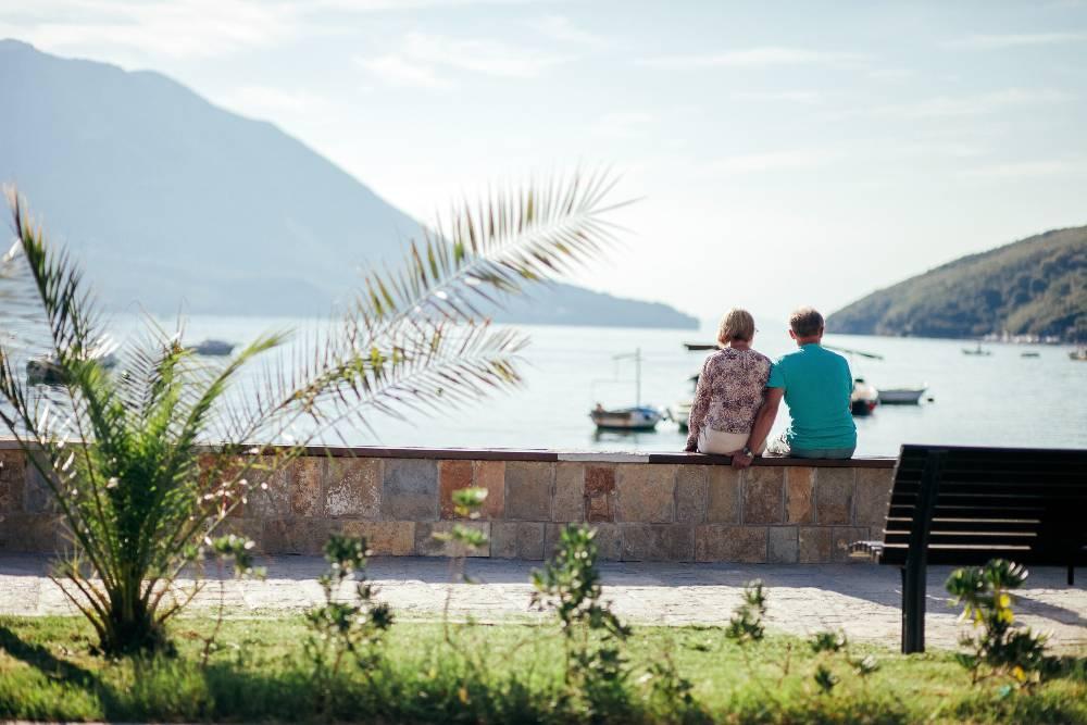 Couple de retraités assis sur un banc admirant un lac au milieu des montagnes