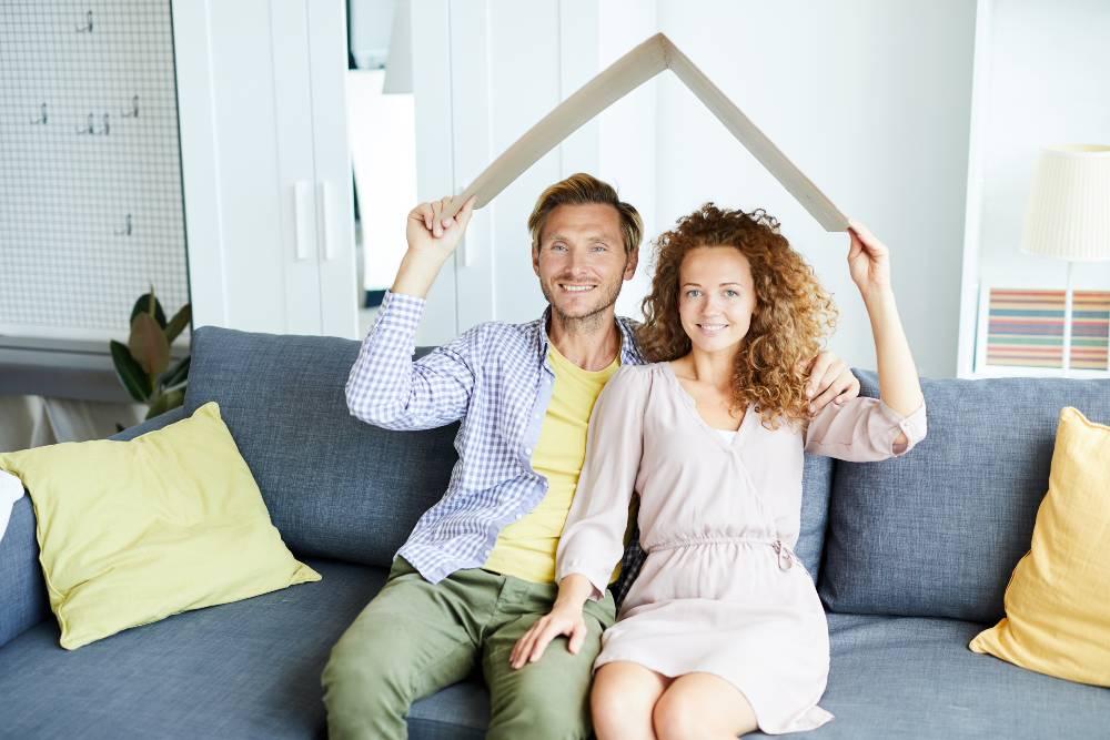 couple assis dans son salon avec un carton plié en forme de toit au dessus de la tête
